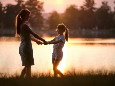 Happy mom and daughter girl relaxing holding hands enjoying time together in summer park at sunset