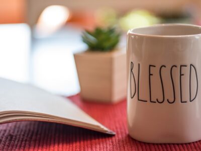 Open book and coffee or tea in a mug that says blessed on the table in morning sunlight
