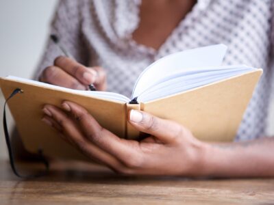 Partial portrait of black female author at home writing in journal