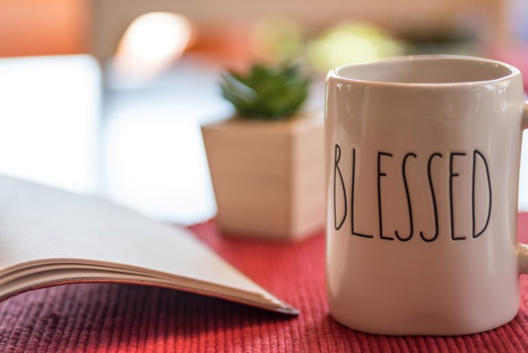 Open book and coffee or tea in a mug that says blessed on the table in morning sunlight